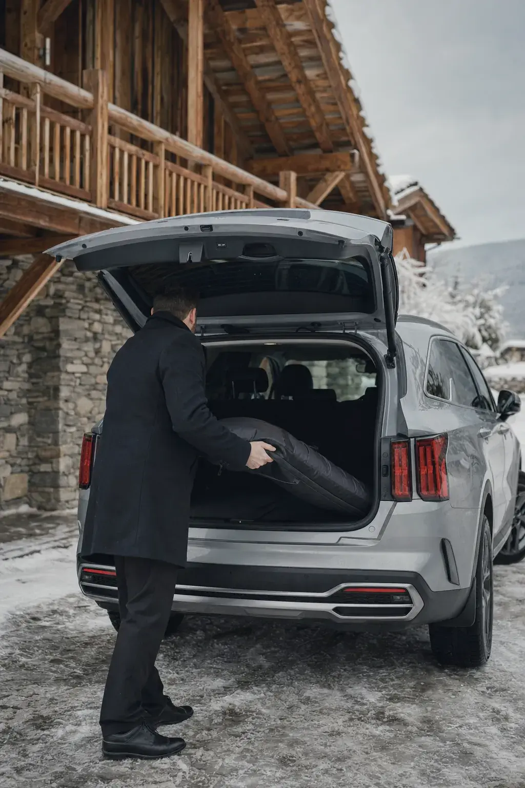 Chauffeur chargeant une housse de skis dans le coffre du SUV devant un chalet enneigé